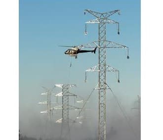 A helicopter strings conductor wire at a transmission tower.