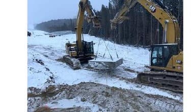 Two excavators install a transmission foundation in the snow-covered right-of-way.